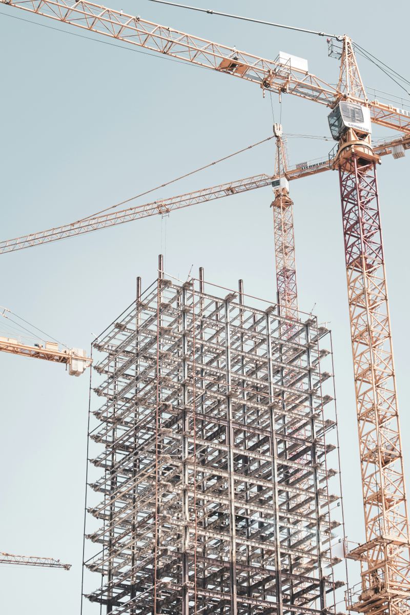 Steel and concrete frame of a new building rising beside two tower cranes