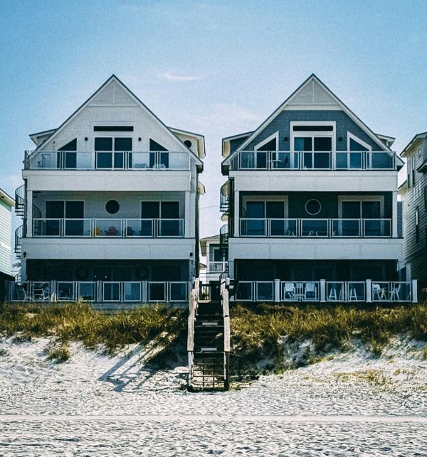 Two shingle-clad oceanfront houses with gabled dormers behind a beach dune